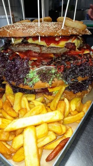 Big Dora in der Seitenansicht mit drei Patties zu je 1.200 g, Ketchup, lila Salat und Pommes auf dem Tablett